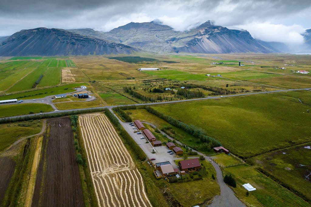 Arnanes Country Hotel Aerial view of farmland with fields, roads, and buildings; mountains and cloudy sky in the background. Hofn South Iceland