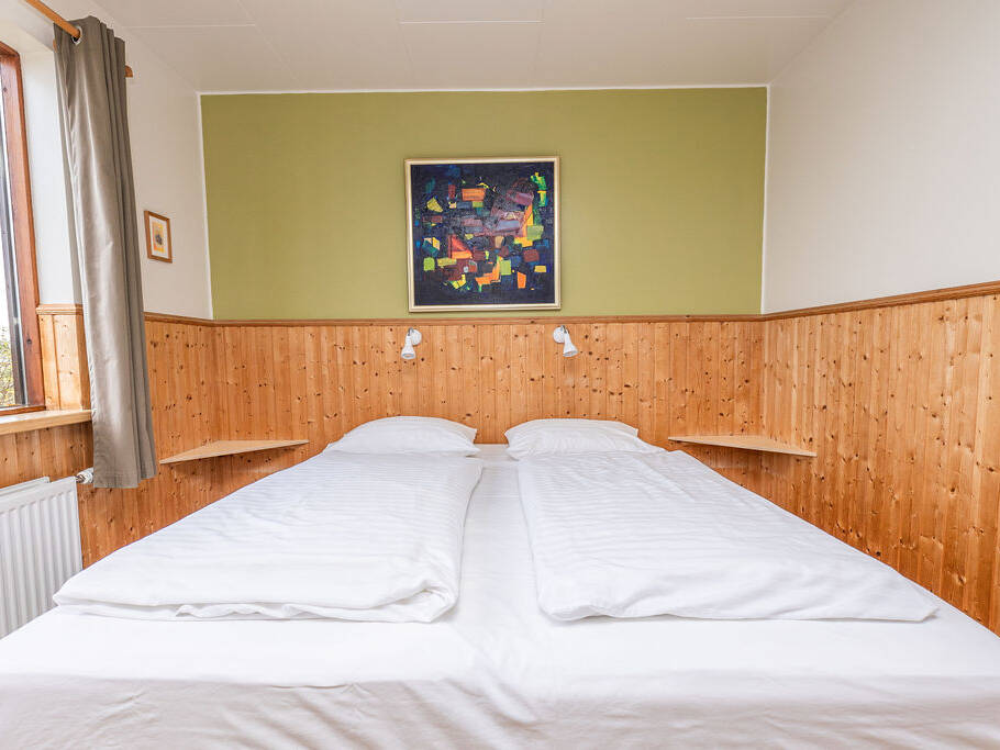Arnanes Country Hotel A small bedroom with two adjoining beds, white bedlinen, wood-panelled walls, a window with a curtain, and a colourful painting above the bed. Hofn South Iceland