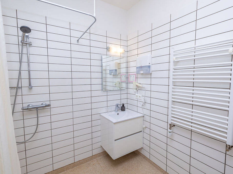 Arnanes Country Hotel Modern white-tiled bathroom with a wall-mounted shower, washbasin with mirror, soap dispenser, and white towel rail. Beige floor and minimal décor. Hofn South Iceland