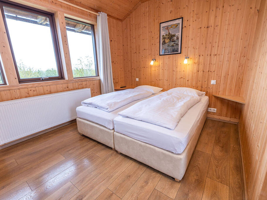 Arnanes Country Hotel A small bedroom with wood-panelled walls, two single beds pushed together, white bedding, wooden floor, two lit wall lamps, a framed picture, and two windows with white curtains. Hofn South Iceland