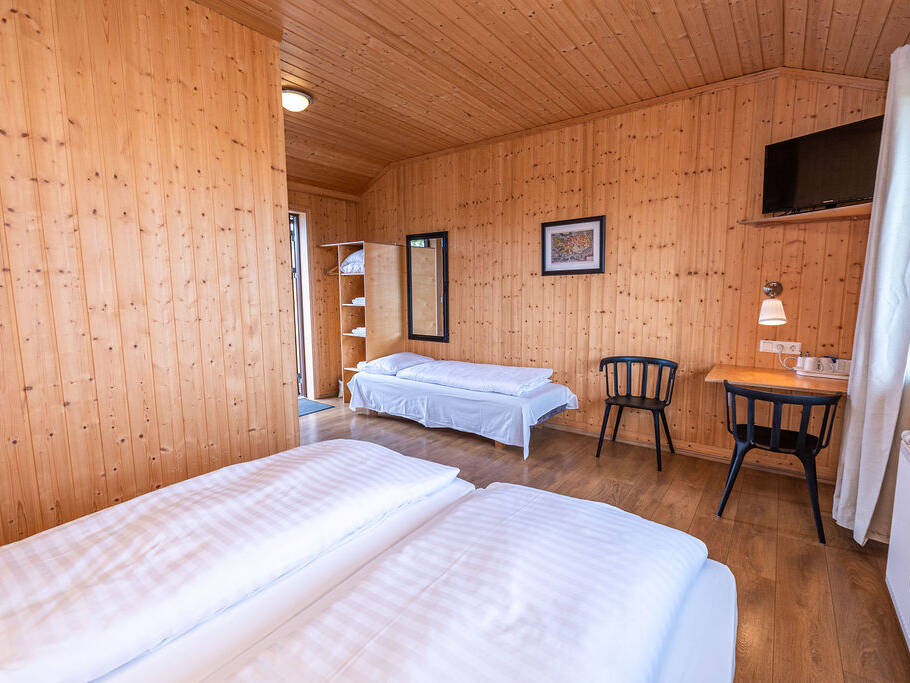 Arnanes Country Hotel Wood-panelled room with two beds, a desk with two chairs, a wall-mounted television, a window with curtains, and a shelf with towels near a doorway. Hofn South Iceland