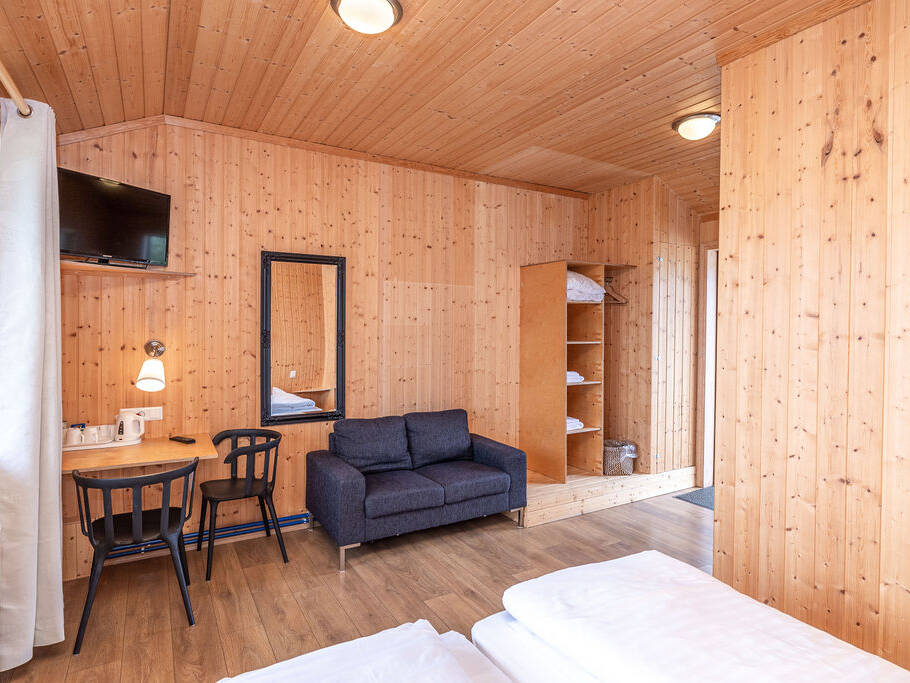 Arnanes Country Hotel A wooden-panelled hotel room with a bed, sofa, desk, chair, wall-mounted TV, mirror, shelving with towels, and a window with white curtains. Hofn South Iceland
