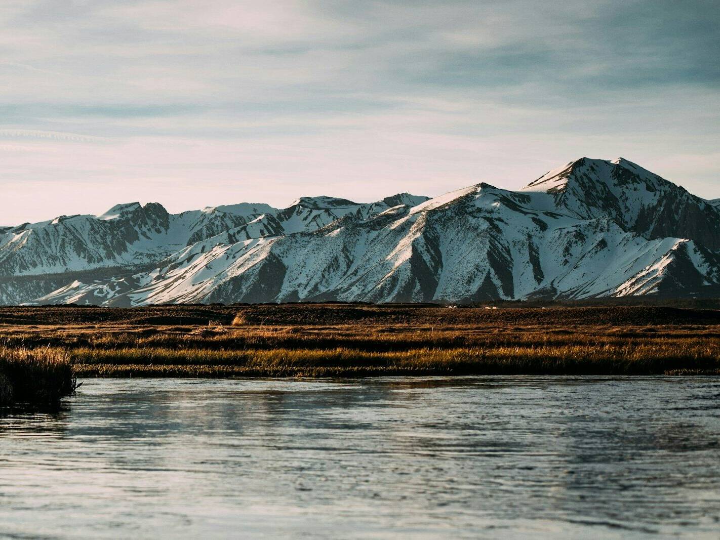 Arnanes Country Hotel A calm river flows in the foreground with snow-capped mountains in the distance under a partly cloudy sky. Hofn South Iceland