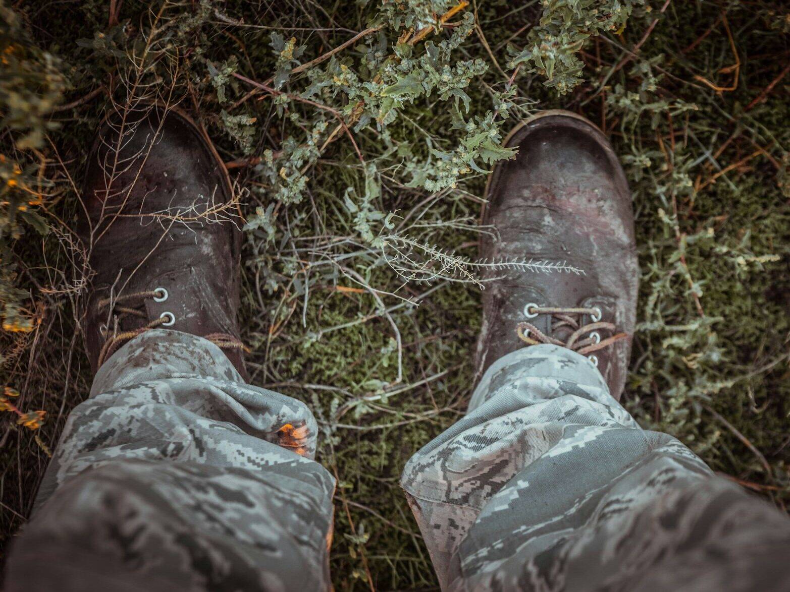 Arnanes Country Hotel A person wearing camouflage trousers and worn dark boots stands on grass and leafy plants, photographed from a top-down perspective. Hofn South Iceland