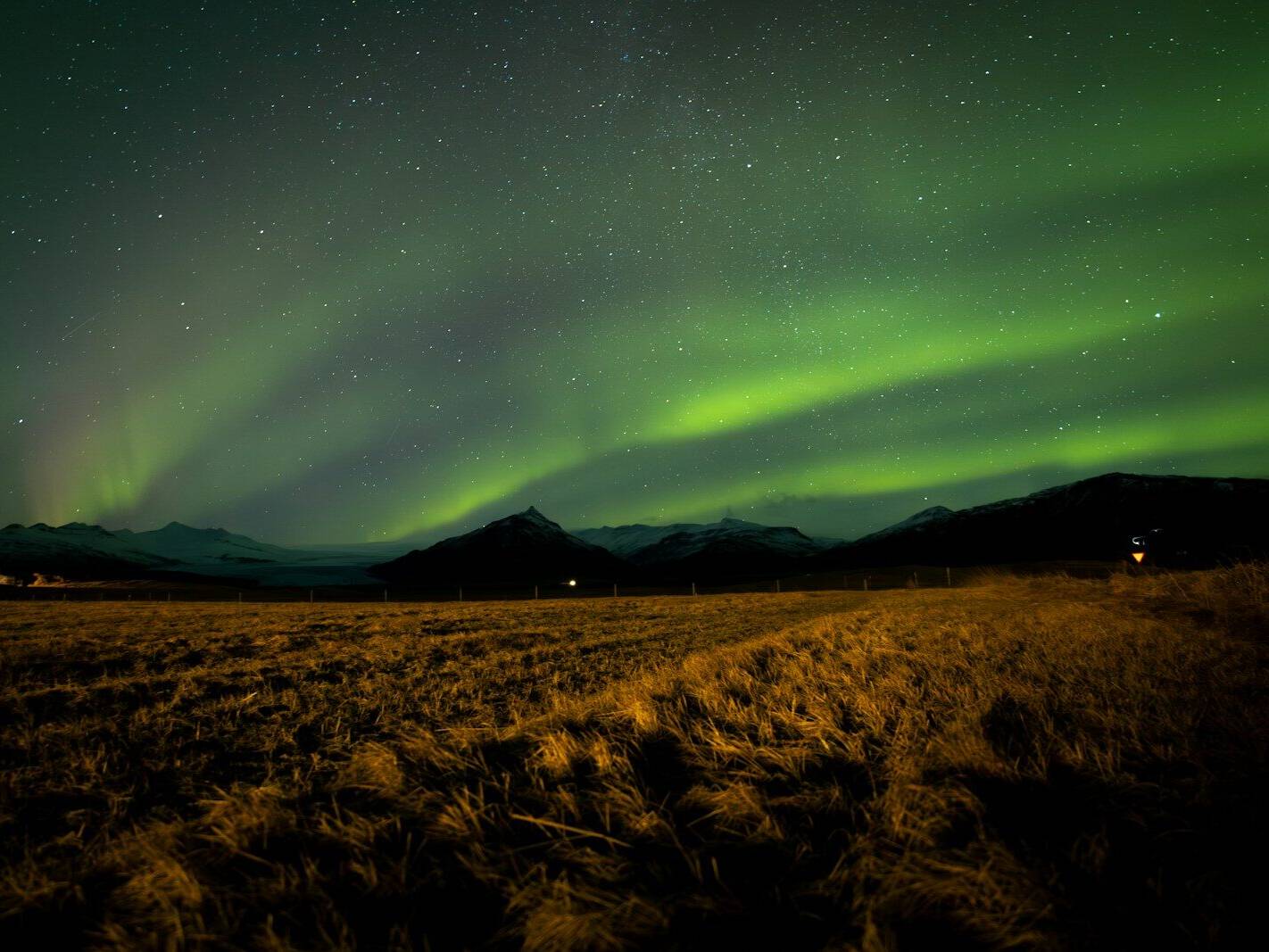 Green aurora borealis over a dark, mountainous landscape.