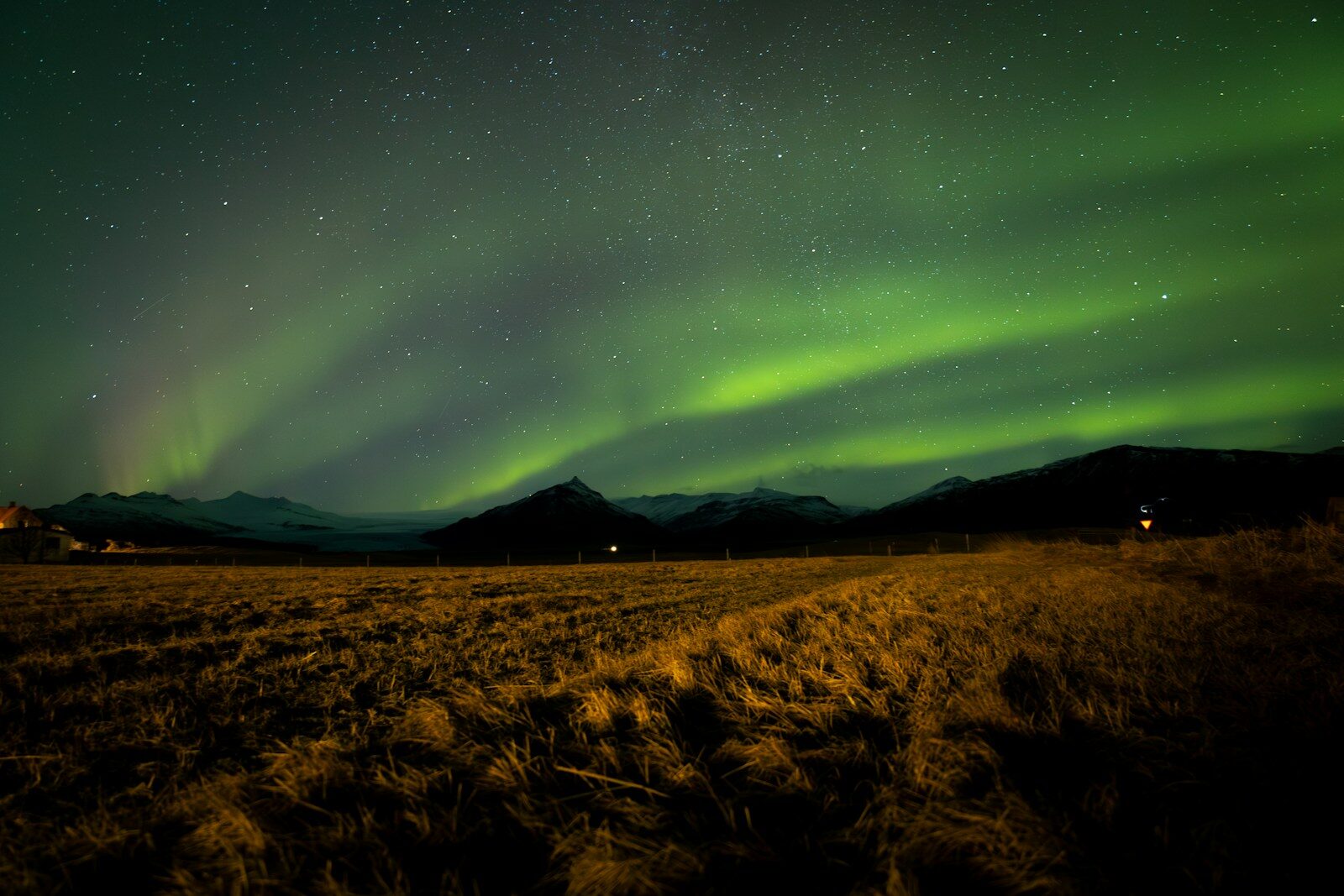 Green aurora borealis over a dark, mountainous landscape.